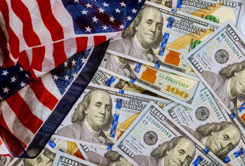 Stacks of the US. one hundred dollar bill closeup and american flag | MCG24 | موقع إلكتروني مغربي شامل متجدد على مدار الساعة