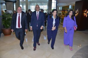 1777201708639 | MCG24 | موقع إلكتروني مغربي شامل متجدد على مدار الساعة Four professionally dressed adults walk together through a bright hotel lobby with glass walls and potted plants nearby.
