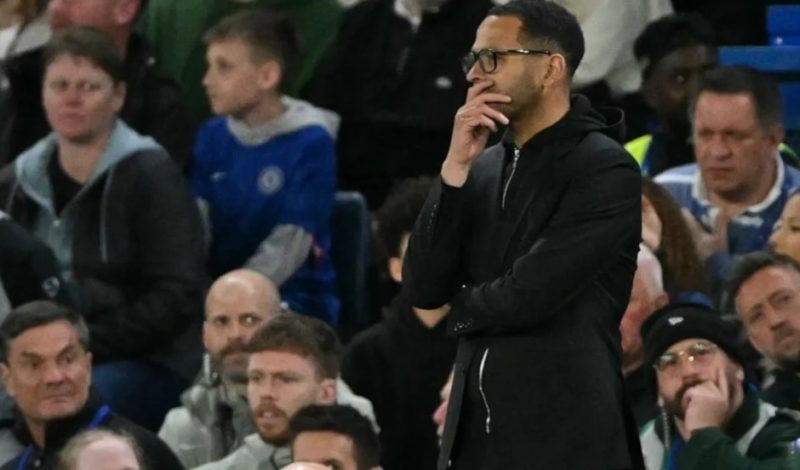 2 | MCG24 | موقع إلكتروني مغربي شامل متجدد على مدار الساعة Man in a black coat and glasses stands with his hand on his chin amid a crowded stadium audience, watching an event.