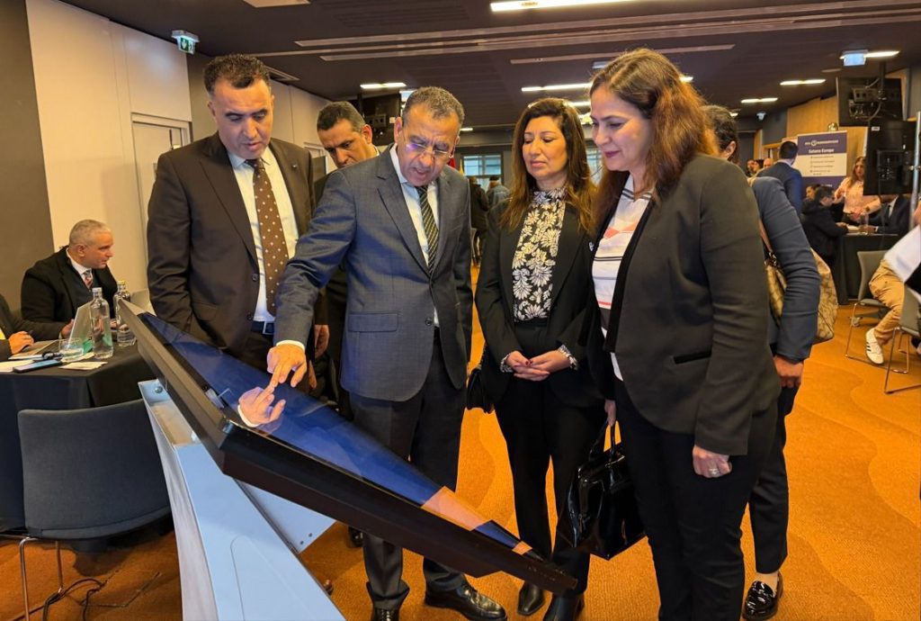 Group of professionals gathered around a large touch screen kiosk at a conference, examining the display.