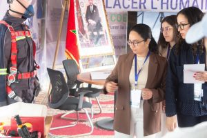 Safety expo booth with a firefighter mannequin in a black suit and red harness; three women with lanyards examine the display.