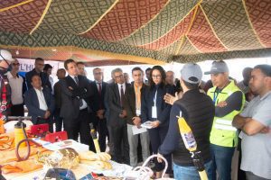 A group of professionals in a tent, listening to a demonstration by a presenter showing safety equipment laid out on a table, including hoses, gloves, and helmets.