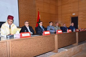 Panel of officials seated at a long desk in a conference room, Moroccan flag visible behind them, each with red nameplates in front of them.