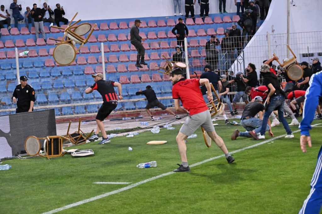 WhatsApp Image 2026-04-19 at 204315 1 | MCG24 | موقع إلكتروني مغربي شامل متجدد على مدار الساعة People on a football field flee as chairs fly through the air during a chaotic incident near the sideline.