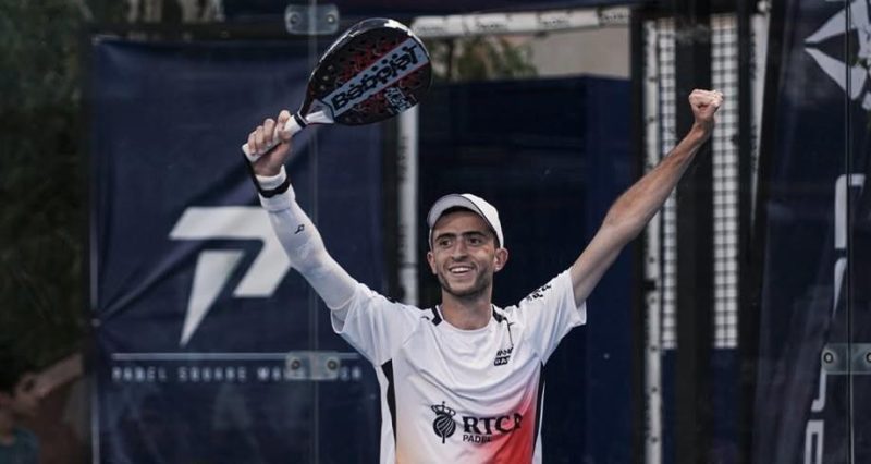 vis_0421202614150703 | MCG24 | موقع إلكتروني مغربي شامل متجدد على مدار الساعة Male padel player in a white shirt and cap raises arms in victory, holding a paddle above his head.