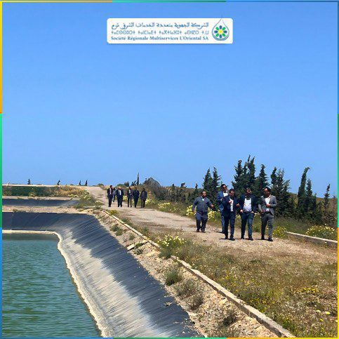 1777675698910 3 | MCG24 | موقع إلكتروني مغربي شامل متجدد على مدار الساعة Group of people walking along a concrete water canal embankment beside a blue sky, sign for Société Régionale Multiservices L'Oriental SA visible overhead (Arabic and French).