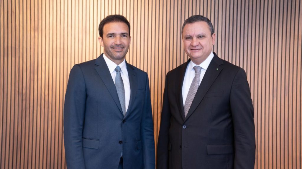 1778785074628 | MCG24 | موقع إلكتروني مغربي شامل متجدد على مدار الساعة Two men in formal suits smiling, standing side by side against a vertical wooden slat wall.