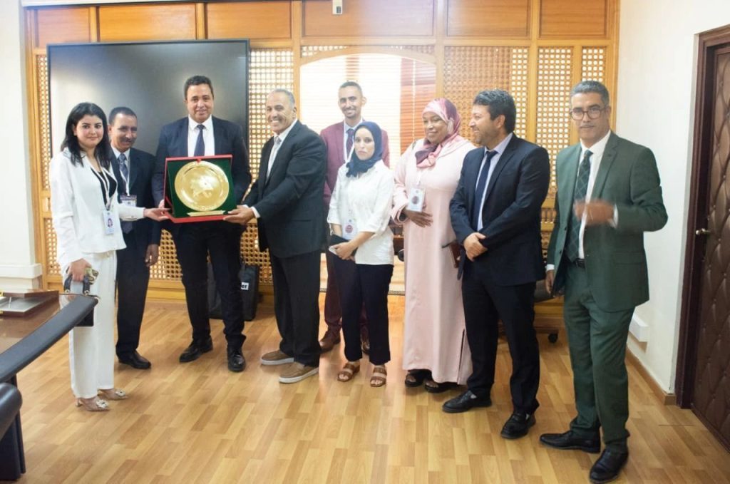1778936331000 | MCG24 | موقع إلكتروني مغربي شامل متجدد على مدار الساعة Group of professionals in business attire pose in an office as a man presents a gold circular award in a red case to a colleague.