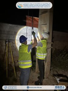 1779451762797 | MCG24 | موقع إلكتروني مغربي شامل متجدد على مدار الساعة Two construction workers in high‑visibility vests and helmets repair a pipe at night, illuminated by a flashlight beam.