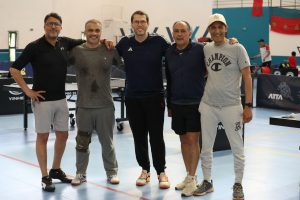 1P2A0055 | MCG24 | موقع إلكتروني مغربي شامل متجدد على مدار الساعة Five men stand with arms around each other in a gym, smiling after a table tennis session.