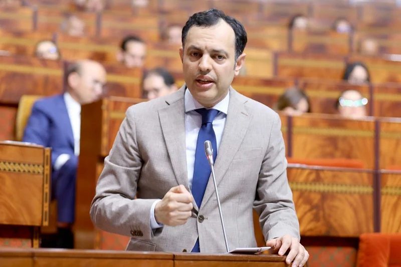 77821026-56525302 | MCG24 | موقع إلكتروني مغربي شامل متجدد على مدار الساعة Man in a gray suit speaks at a podium with a microphone in a wood-paneled parliamentary chamber.