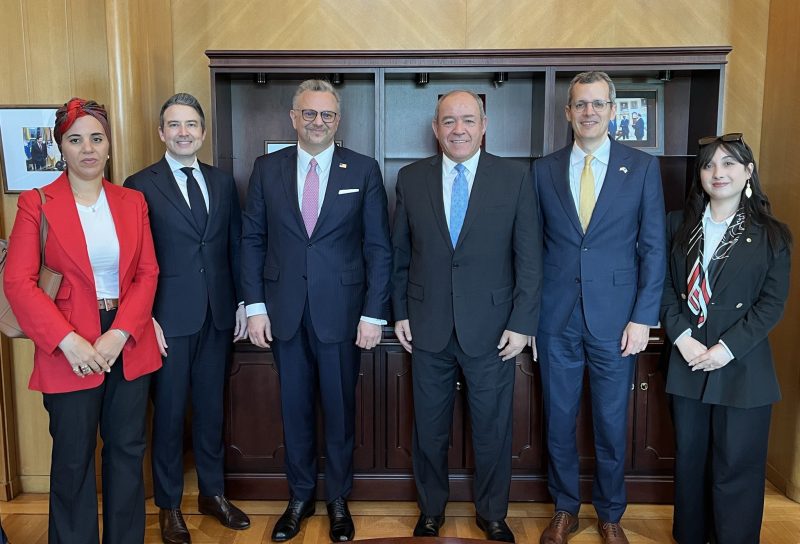 Six professionally dressed individuals standing side by side in a wood-paneled office, smiling at the camera.