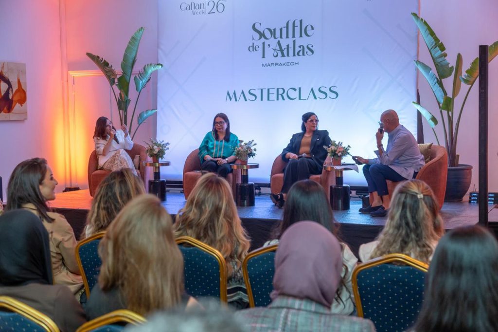 مراكش تحتفي بـ “نفس الأطلس” من خلال “أسبوع القفطان” Panel discussion on a stage with four speakers seated in orange chairs, audience listening attentively.