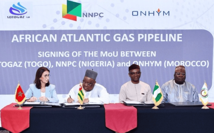 Gazoduc_Nigeria-Maroc | MCG24 | موقع إلكتروني مغربي شامل متجدد على مدار الساعة Four officials sign a MoU at a long table with red table runners, flags, and a blue backdrop reading 'AFRICAN ATLANTIC GAS PIPELINE'.