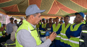 Gemini_Generated_Image_irdz7dirdz7dirdz | MCG24 | موقع إلكتروني مغربي شامل متجدد على مدار الساعة Trainer in a neon safety vest demonstrates a respirator to a group of workers in reflective vests under a patterned canopy.