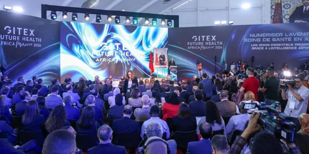 Gitex-Future-Health-Africa-2026 | MCG24 | موقع إلكتروني مغربي شامل متجدد على مدار الساعة Stage at a large conference with blue, swirling backdrop reading 'GITEX Future Health Africa Morocco 2026' and a seated audience in front of a presenter podium.