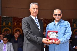 IMG-20260516-WA0022 | MCG24 | موقع إلكتروني مغربي شامل متجدد على مدار الساعة A man in a dark suit presents a plaque to a man in a blue denim shirt during an awards ceremony, with seated attendees in the background.