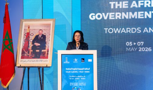 Speaker at a podium during an Africa government conference, with Moroccan flag and a framed portrait beside the stage.