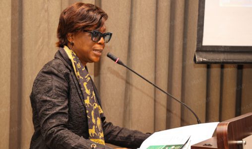Nouveau-projet1170 | MCG24 | موقع إلكتروني مغربي شامل متجدد على مدار الساعة African American woman in a black jacket and patterned scarf speaking at a podium with a microphone during a presentation.
