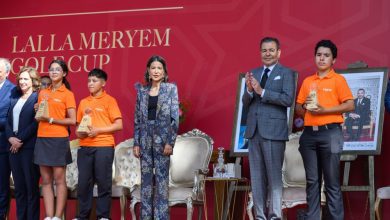 Young award recipients in orange shirts hold trophies on stage beside suited officials against a red backdrop of the ceremony.