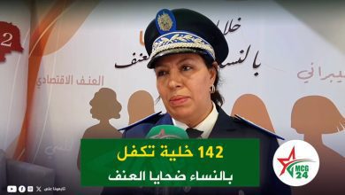 Police spokeswoman in uniform speaking at a press conference, microphone in front, Arabic backdrop and MCG 24 logo.