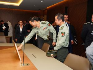 Two military officers in uniform place a card at a conference table as others stand nearby in a formal room.