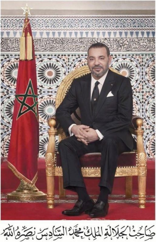 WhatsApp-Image-2026-05-26-at-1217041-579x900jpeg-579x900 | MCG24 | موقع إلكتروني مغربي شامل متجدد على مدار الساعة Portrait of a man in a dark suit seated on an ornate gold chair beside a Moroccan flag, with Arabic script below.