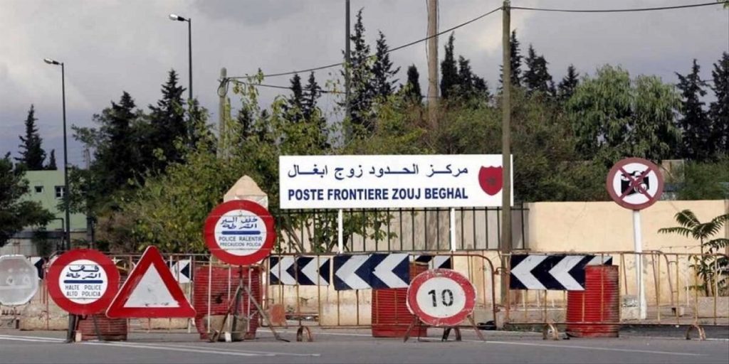 Border crossing with multiple construction barriers and traffic signs, including a 10 km/h speed sign and no-entry/stop signs, under a sign reading 'Poste Frontière Zouj Beghal' in Arabic and French.
