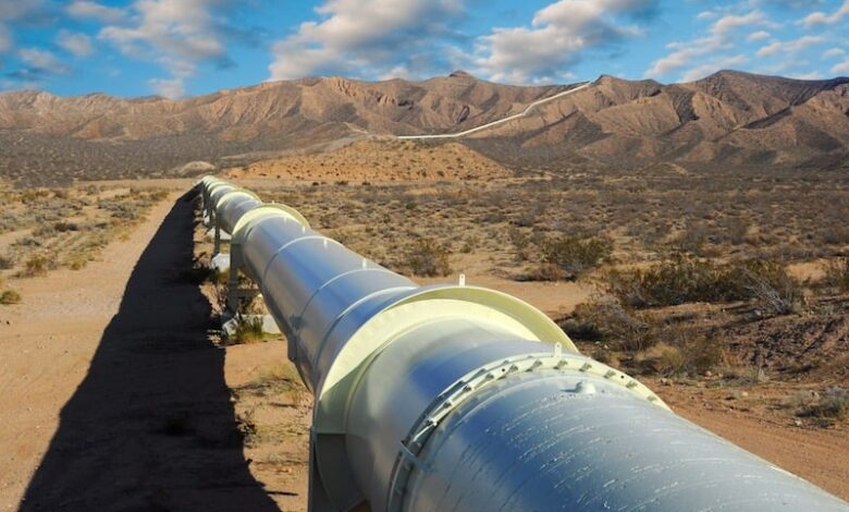 gaz-algerie-780x470 | MCG24 | موقع إلكتروني مغربي شامل متجدد على مدار الساعة Long white industrial pipeline stretches across a dry desert landscape toward rocky hills under a blue sky.