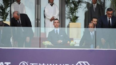 Man in a dark suit seated at a glass barrier during a formal event, with others standing behind, in front of a purple banner reading Wanda Diamonds.