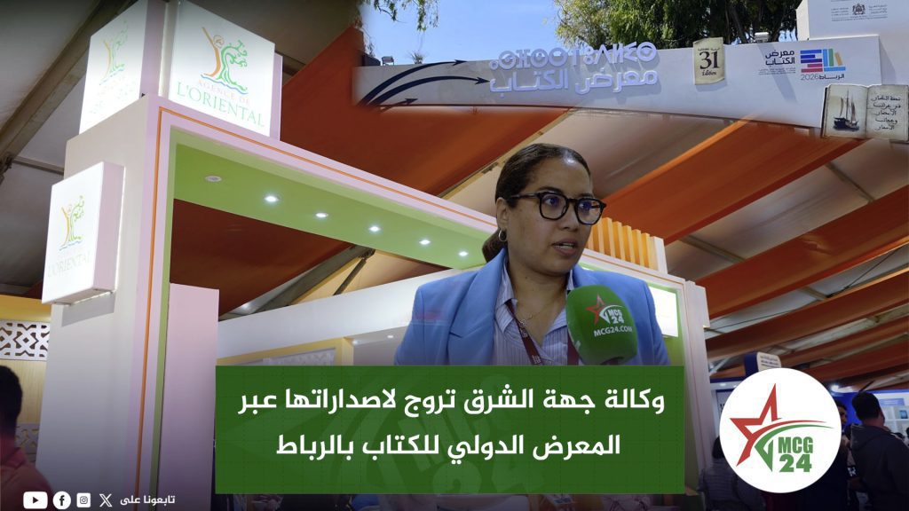 وكالة جهة الشرق تروج لاصداراتها عبر المعرض الدولي للكتاب بالرباط Woman with glasses speaking into a green microphone at a booth at a book fair; MCG24 logo visible, Arabic text overlay on a green banner in front of her.