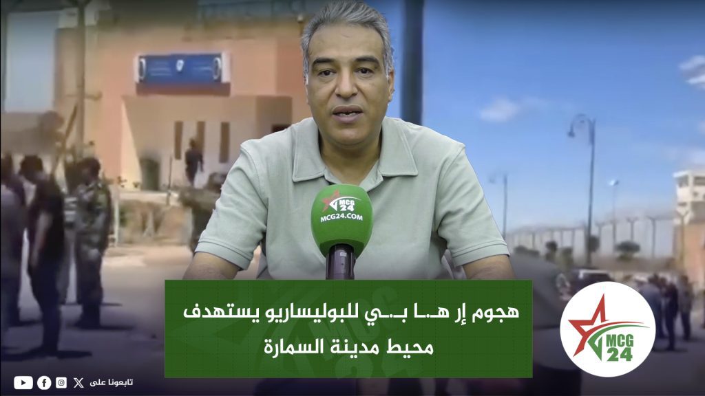 هجوم إر هـ.ـا بـ.ـي للبوليساريو يستهدف محيط مدينة السمارة News anchor speaks into a green MCG24 microphone with an Arabic headline banner on a city backdrop behind him.