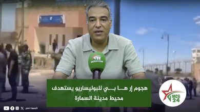 News anchor speaks into a green MCG24 microphone with an Arabic headline banner on a city backdrop behind him.