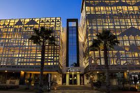 téléchargement 38 | MCG24 | موقع إلكتروني مغربي شامل متجدد على مدار الساعة Exterior of a modern glass office building at dusk with palm trees lining the entrance.