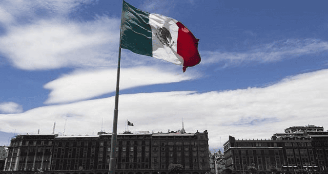 515155454541 | MCG24 | موقع إلكتروني مغربي شامل متجدد على مدار الساعة Mexican flag waving atop a tall flagpole in front of a large government building under a blue sky.