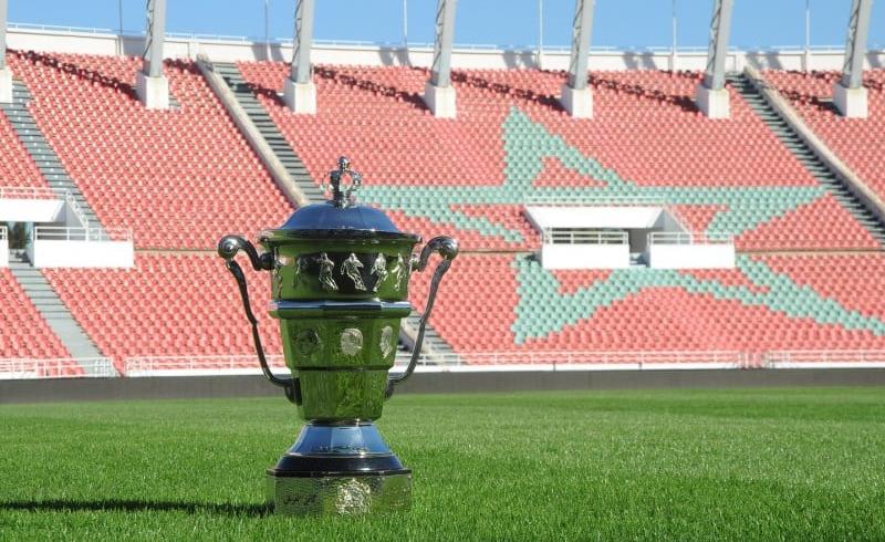 vis_0322202415075411 | MCG24 | موقع إلكتروني مغربي شامل متجدد على مدار الساعة Polished trophy on a green soccer field with red stadium seats and a large turquoise star design in the background.