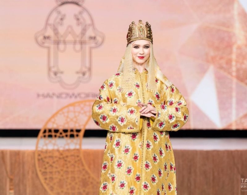 القفطان روسيا | MCG24 | موقع إلكتروني مغربي شامل متجدد على مدار الساعة Model in a gold-embroidered traditional robe with a crown and veil on a runway stage.