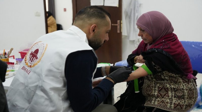 بيت-مال-القدس-حملة-طبية | MCG24 | موقع إلكتروني مغربي شامل متجدد على مدار الساعة Healthcare worker wearing a white vest administers a vaccination to a seated woman wearing a pink hijab in a clinic setting.