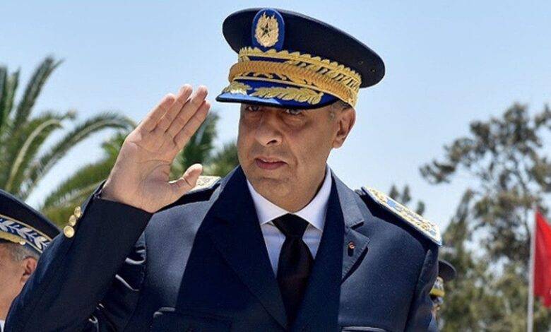 عبد-اللطيف-حموشي-780x470 | MCG24 | موقع إلكتروني مغربي شامل متجدد على مدار الساعة Male military officer in dress uniform saluting, wearing a dark blue peaked cap with gold braid, outdoors with palm trees in the background.