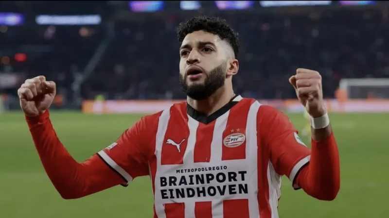 260408092037 | MCG24 | موقع إلكتروني مغربي شامل متجدد على مدار الساعة PSV Eindhoven player in red-and-white striped kit celebrates with fists raised on the pitch, Brainport Eindhoven sponsor on jersey.