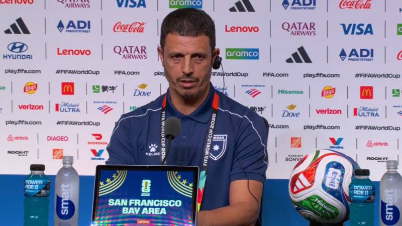 6a326fd8fe191bd3077e9030_default | MCG24 | موقع إلكتروني مغربي شامل متجدد على مدار الساعة Coach at a FIFA World Cup press conference, seated with a laptop displaying 'San Francisco Bay Area' and a soccer ball on the table, backdrop full of sponsor logos.