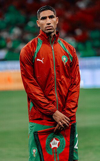 Moroccan national football team player wearing a red-green training jacket on a soccer field.