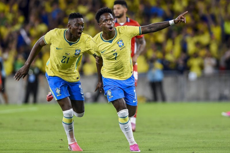 GettyImages-2278485465 | MCG24 | موقع إلكتروني مغربي شامل متجدد على مدار الساعة Two Brazil players celebrate a goal, wearing yellow jerseys and blue shorts on a grass pitch with a cheering crowd in yellow in the background, one pointing ahead.