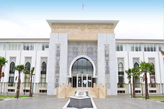 IMG-20260613-WA00451 | MCG24 | موقع إلكتروني مغربي شامل متجدد على مدار الساعة Front view of a modern government building with an arched entrance, palm trees, and a central fountain in front.
