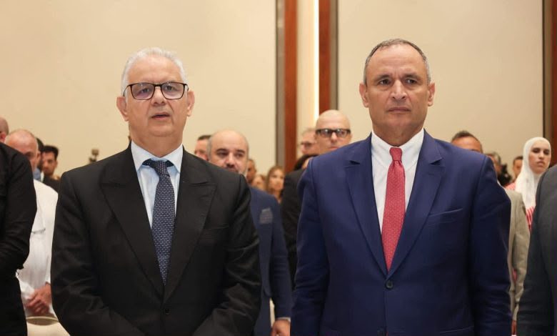 IMG-20260615-WA0096 | MCG24 | موقع إلكتروني مغربي شامل متجدد على مدار الساعة Two men in business suits standing at a formal event, with a crowd of attendees behind them in a conference hall.