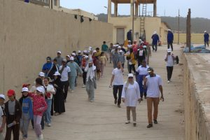 IMG-20260616-WA0004 | MCG24 | موقع إلكتروني مغربي شامل متجدد على مدار الساعة Large crowd of children and adults walking along a concrete path beside a tall beige wall, many wearing white caps.