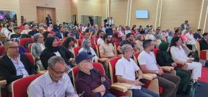 Diverse audience seated in red theater-style chairs listening to a talk in a modern conference hall.