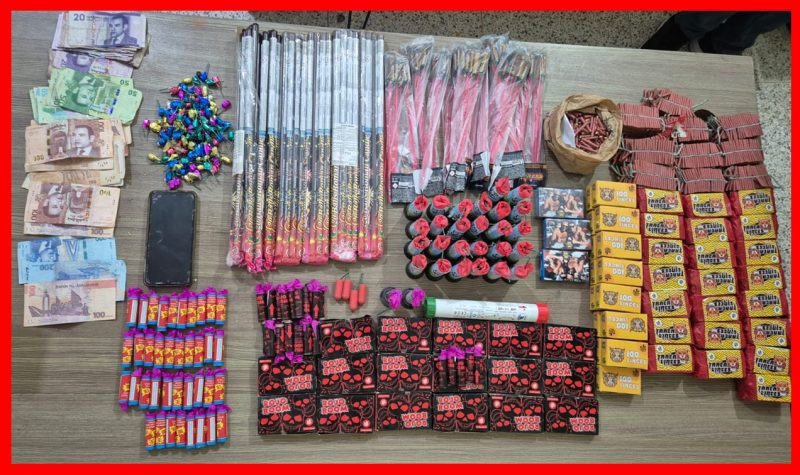 Display of seized items on a table: bundled cash, a smartphone, colorful wrapped fireworks and various packaged goods arranged in rows as evidence.