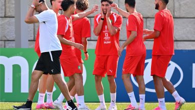 Soccer teammates in red uniforms celebrate together on a grassy field during training.