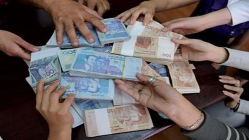 MCAJ57FYZBFUZC34FAX75AYY6I | MCG24 | موقع إلكتروني مغربي شامل متجدد على مدار الساعة Several hands surround and reach for a pile of stacked currency on a table.